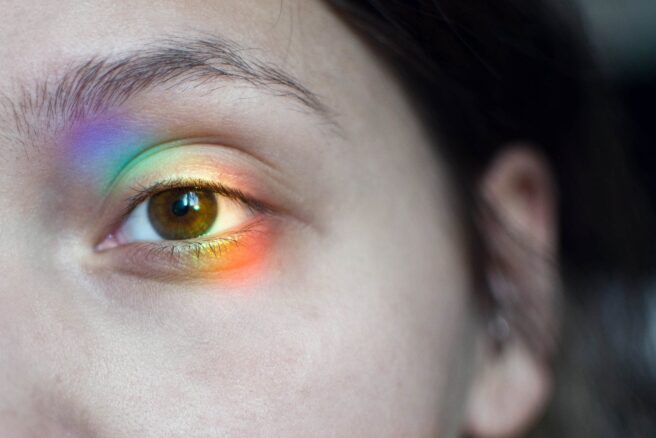 Mustavalkoinen osakuva kasvoista, jossa sateenkaaren värinen heijastus silmän kohdalla