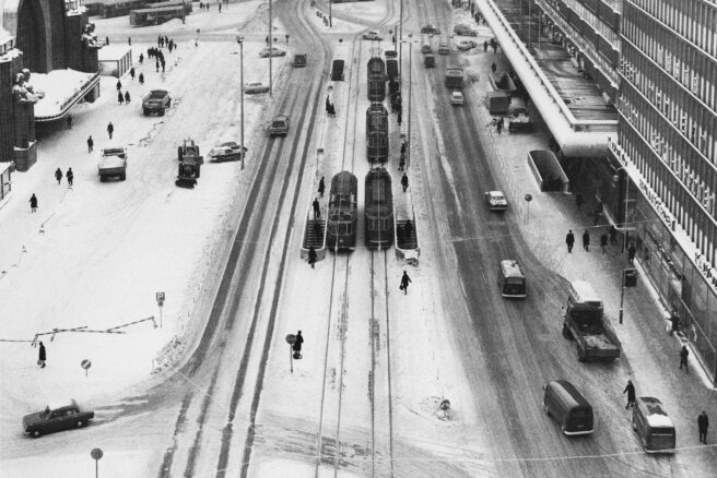 Mustavalkoinen kuva Helsingin Kaivokadulta, jossa busseja, autoja ja jalankulkijoita