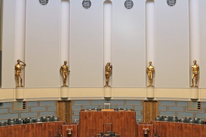 Sisäkuva eduskuntalaon istuntosalista, Wäinö Aaltosen patsaat katsovat seinältä saliin