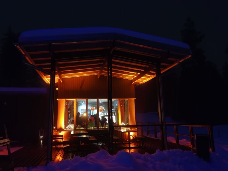 Talvinen hämärä kuva kahvilan ikkunasta sisään, pöydän ääressä on ihmisiä kokoontuneena keskustelemaan