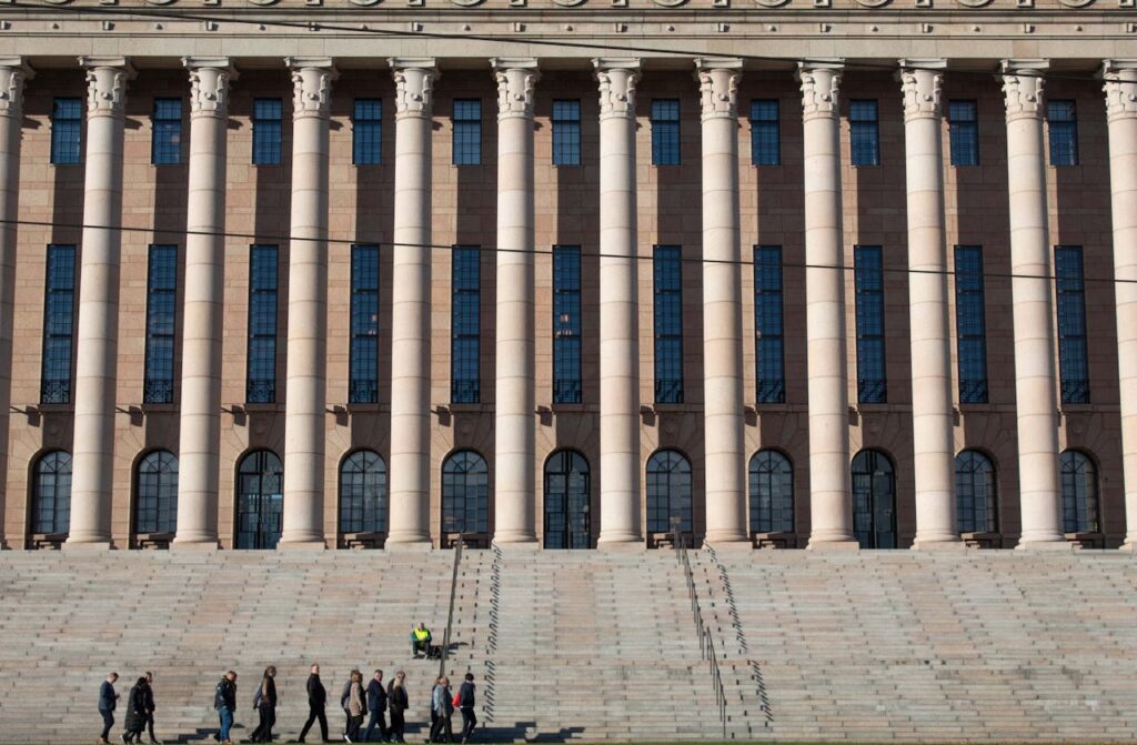 Eduskuntatalon julkisivu, etualalla pieni joukko ihmisiä